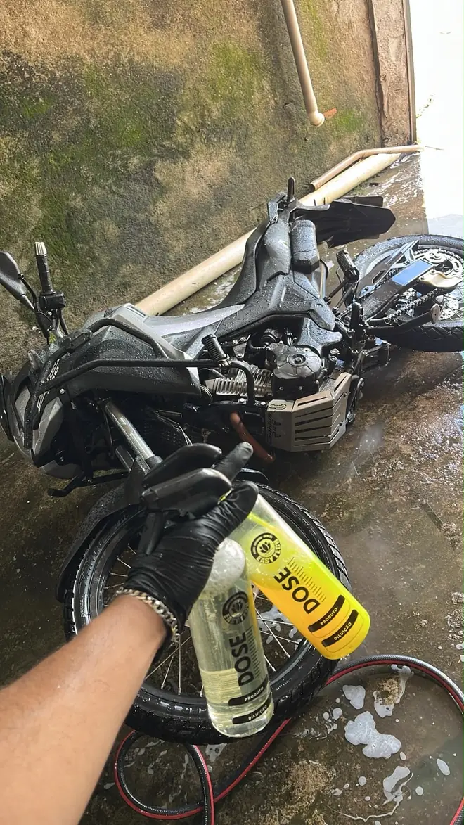Mão de luva aplicando produto amarelo na roda de uma moto